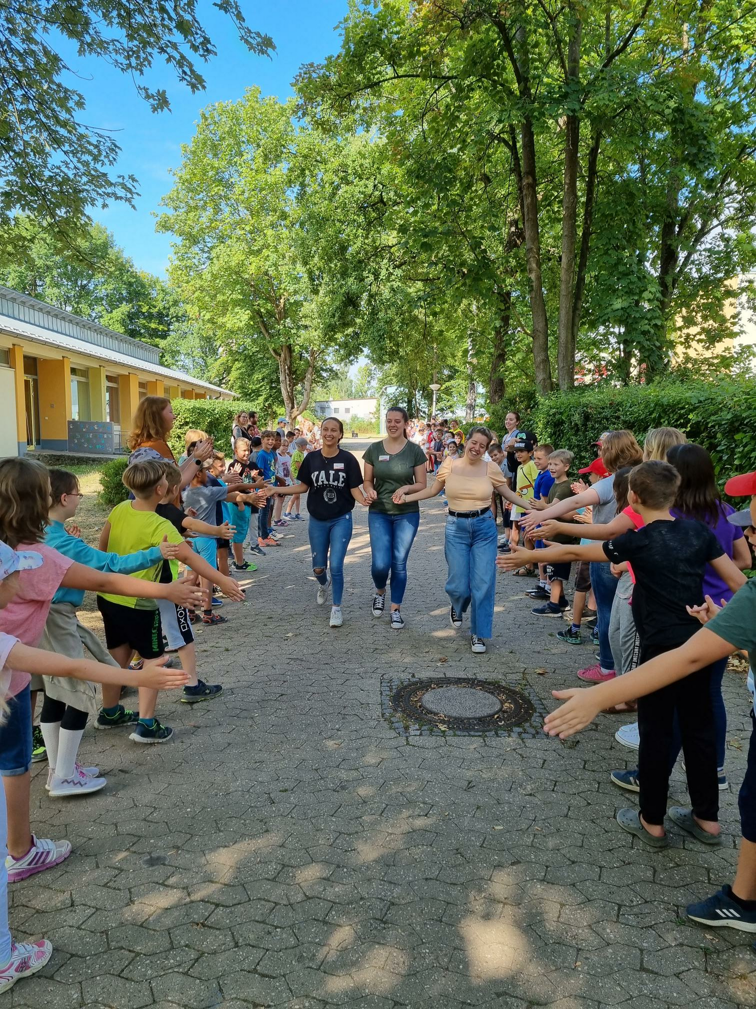 Drei Erwachsene in der Mitte. Schülerinnen und Schüler stehen Spalier.